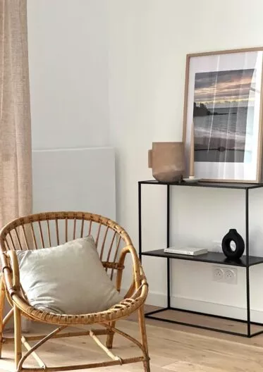 Appartement témoin de la résidence Chemin de la Mer à Dinard. Fauteuil et étagère dans un espace de vie spacieux à la décoration bord de mer.