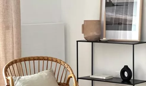 Appartement témoin de la résidence Chemin de la Mer à Dinard. Fauteuil et étagère dans un espace de vie spacieux à la décoration bord de mer.