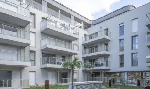 Immeuble résidentiel "esprit du large" moderne avec balcons en verre et palmiers au rez-de-chaussée