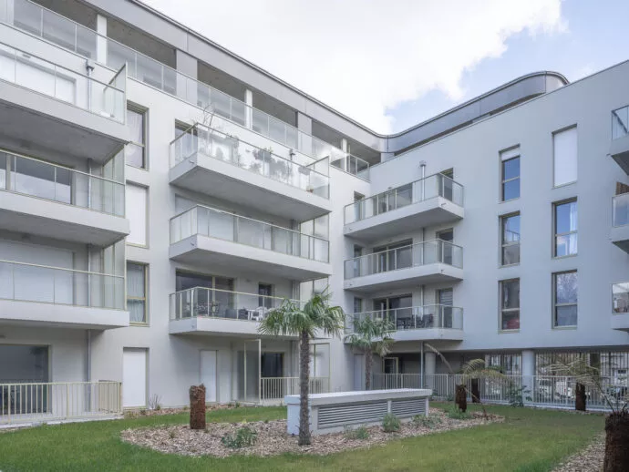 Immeuble résidentiel "esprit du large" moderne avec balcons en verre et palmiers au rez-de-chaussée