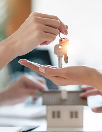 Remise/échange des clés entre deux personnes. Arrière plan on aperçoit une maison.
