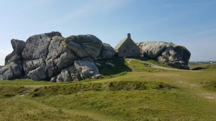 Chaumière bretonne en haut d'une colline bordée d'herbes vertes.
