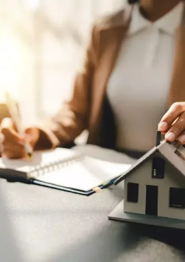 Conseillère immobilière tenant une maison miniature et prenant des notes à son bureau