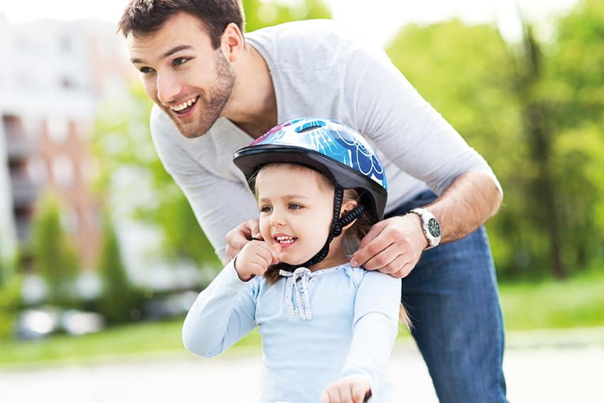 Father helping daughter with bike helmet
